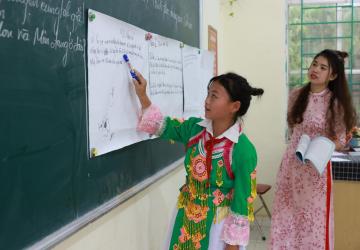 A young girl is writing on a black board in a classroom