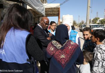 The Resident Coordinator is standing in the middle of a group of people and listening to them