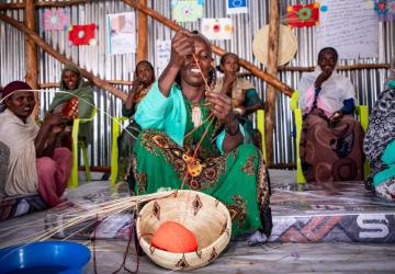 A group of women in colorful traditional clothing are gathered in a circle weaving.