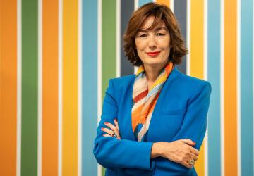 A woman in a blue work suit poses in front of a colorful background.