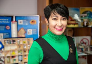 A woman wearing a green top and blue blazer looks at the camera and smiles 
