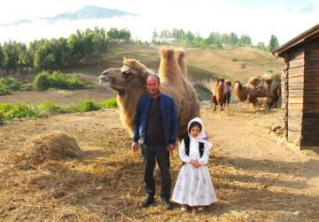 A man with his daughter with a camel in the background