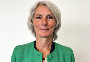 The RC is wearing a green jacket and looking at the camera, standing in front of a white background