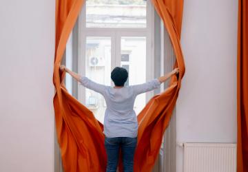 A Georgian woman opens a curtain.