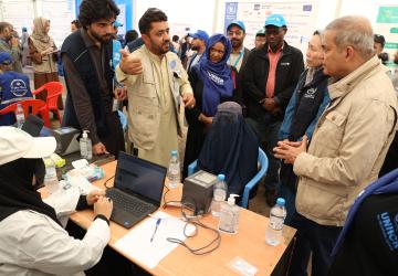 A man is asking another one a question, while there are crows around them. There is also a woman on a computer. 