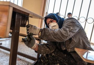 A woman in Iraq refurbishes a desk in a classroom.