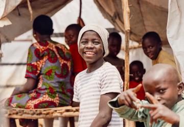 A young boy in Burundi smiles for a photo while surrounded by friends and siblings.