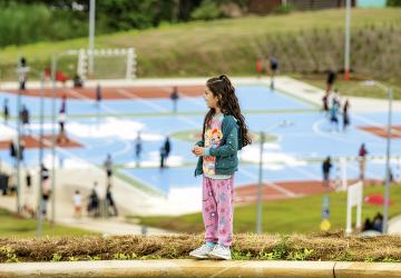 A girl in Costa Rica stands on a hill overlooking a basketball court.