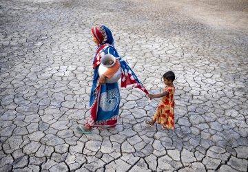 A woman in Bangladesh walks on drought-stricken land while holding her daughter's hand.