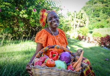 A woman in Dominica sits in front of a basket of food.