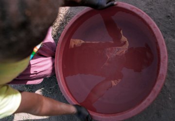 A child in South Sudan looks at his reflection in a bucket of water.
