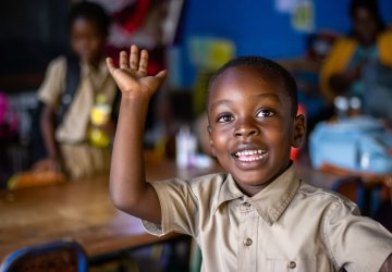 A young students raises his hand in a classroom in Jamaica.