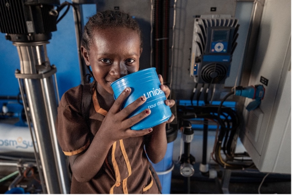 young child drinks water from a blue cup 
