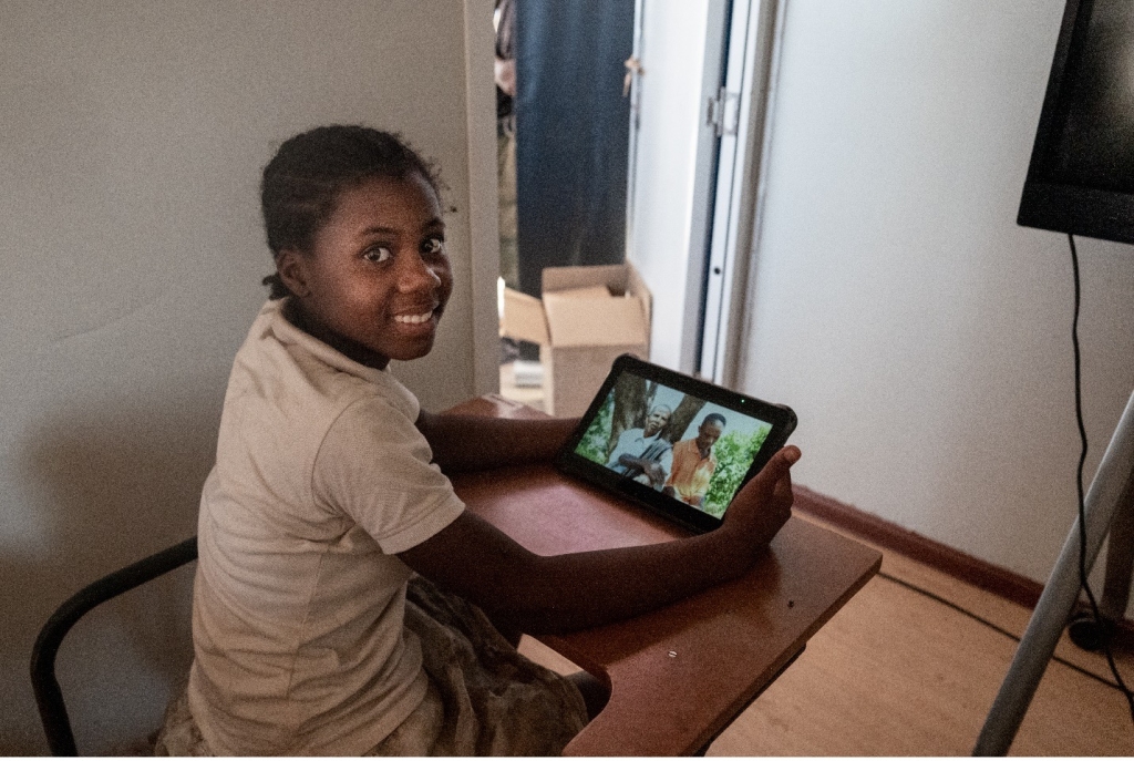 young girl sits at a desk using tablet 