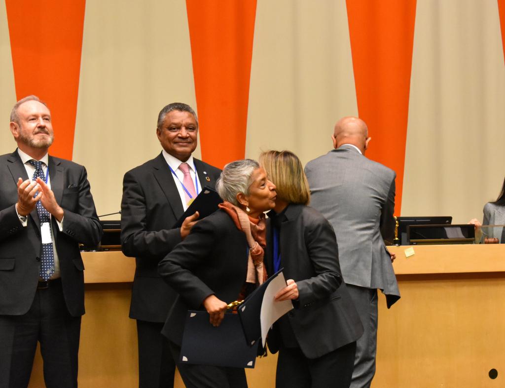 two women in suits hug on stage wile receiving an award 
