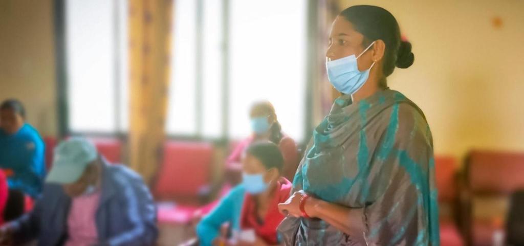 Woman in traditional Indian dress and face mask, in a room with other people, representing disability awareness and accessibility. 