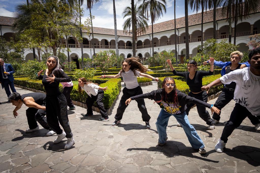 A group of young people are having a dance presentation in an outdoor area surrounded by bushes and trees.