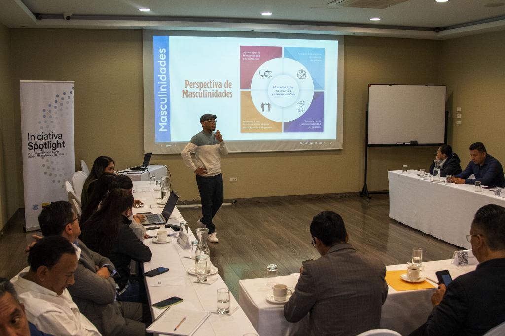 A group of people are sitting around a conference room while a man is standing and presenting.