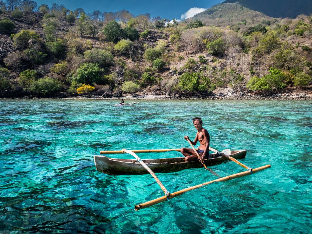 A man in a makeshift boat paddles through a blue lagoon in Indonesia