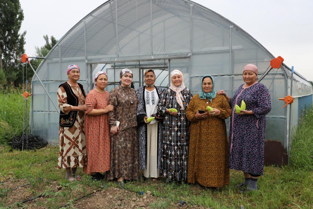 A group of women standing outdoors holding agricultural produce 