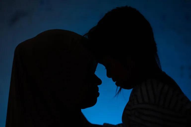 The silhouette of a mother embracing her young daughter.