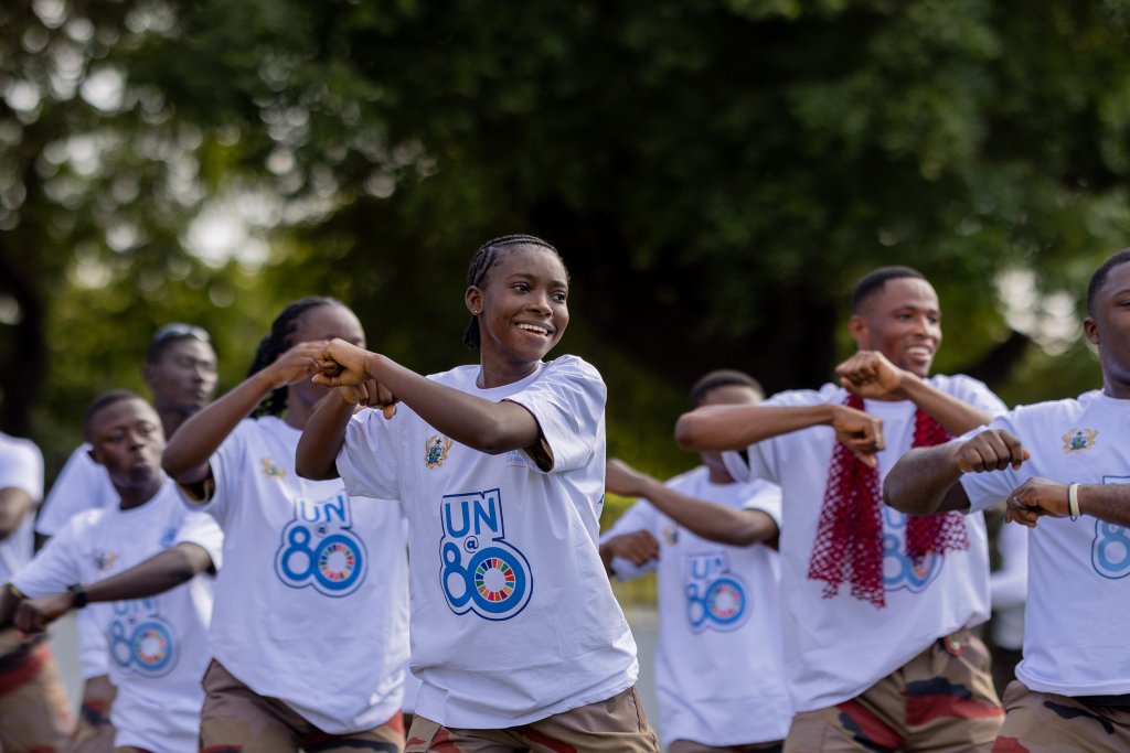 A group of people in matching UN-themed shirts perform a synchronized outdoor dance during a community event.