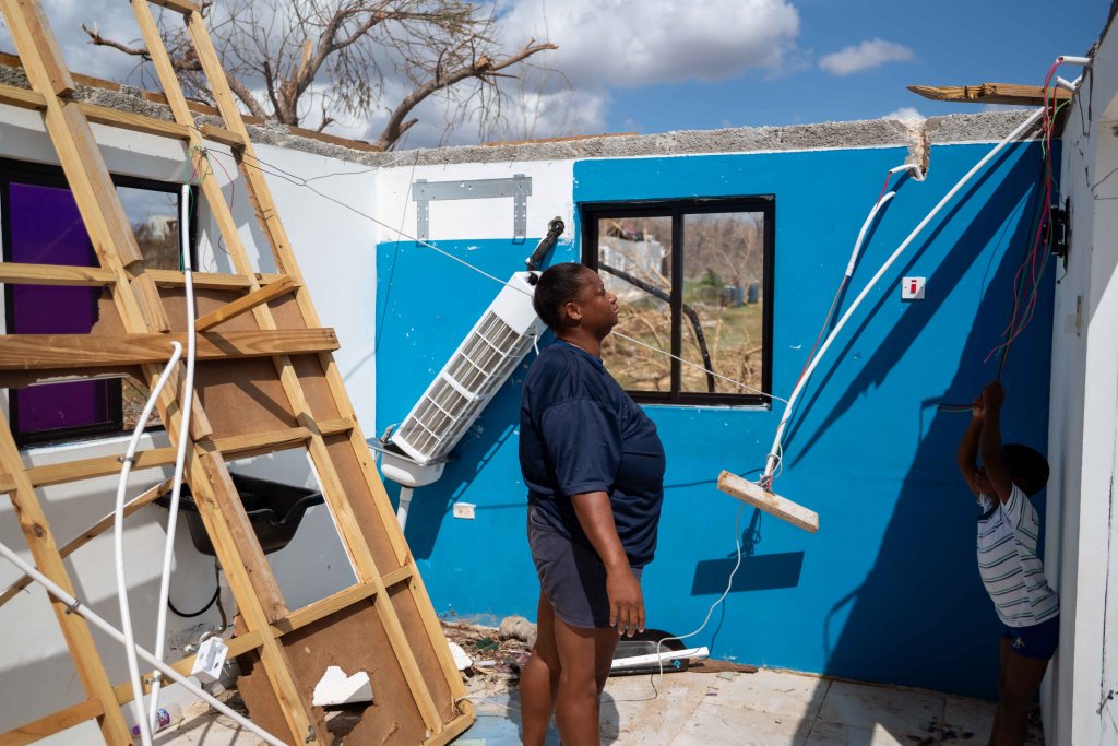 A woman in Jamaica stands in a destroyed house with her son.