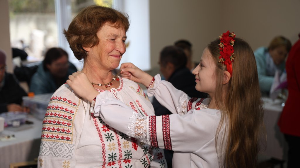 A girl in Moldova puts a necklace around an elderly woman's neck.