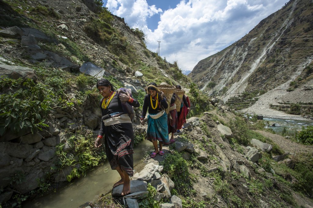 Three women in Nepal walk on a small cliff.