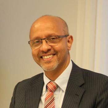 A smiling man in a suit looks directly at the camera.