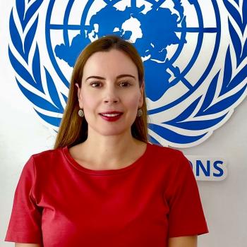 A woman in a red dress stands in front of the United Nations logo.