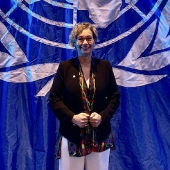 A woman stands in front of the United Nations Flag.