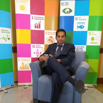 A man sits on a chair near a sign of the sustainable development goals.