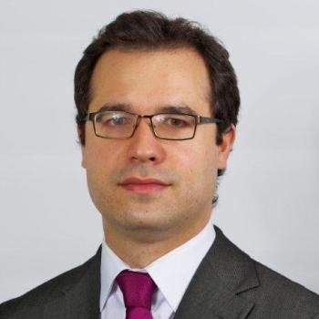 A man in a red tie and white shirt looks directly at the camera. 