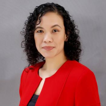 A woman in a red jacket looks directly at the camera.