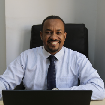 A smiling man sits in front of a laptop computer. 