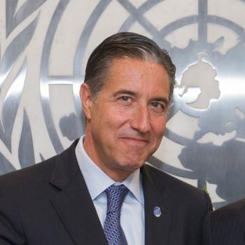 A man grins near the United Nations logo.