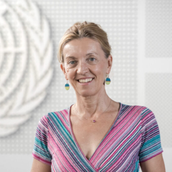 A woman in a colorful dress stands in front of a white United Nations logo