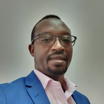 A man in a blue suit and pink shirt looks down at the camera.