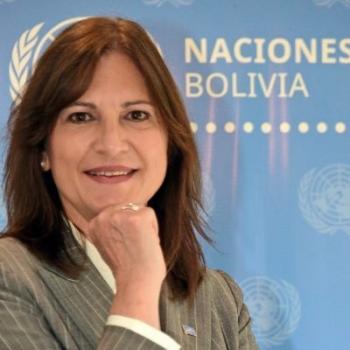 A woman with her hand on her chin stands in front of the United Nations Bolivia logo.