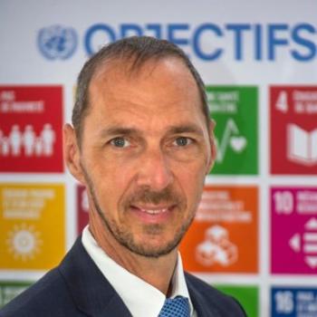 A man smiles at the camera in front of the Sustainable Development Goals.