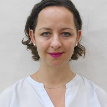 An image of a woman with a white shirt and pink lipstick looking directly at the camera.