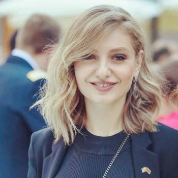 woman in dark suit and blonde hair smiles to camera
