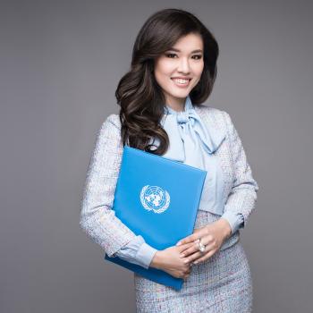 woman in light coloured suit stands holding a UN folder 
