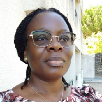 A woman in spectacled glasses and a flowered shirt stands outside and looks ahead.