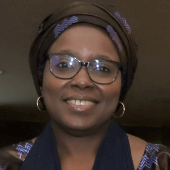 A woman in a chic headwrap, glasses, and gold hoops smiles and looks straight on at the camera.