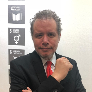 man in black suit and red tie stands in front of the camera 