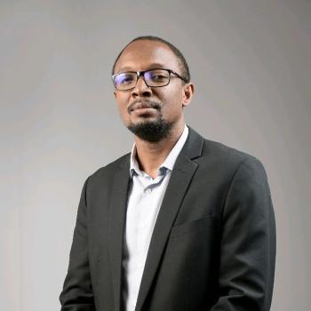 man in black suit and white shirt looks towards camera 