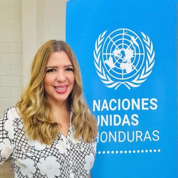 woman in pattern shirt and long hair stands in front of UN sign 