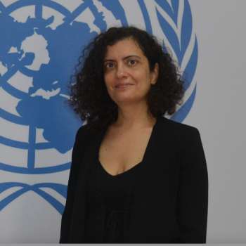 woman in dark suit dark stands in front of UN emblem 